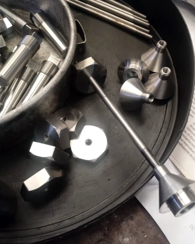 Piezas torneadas de acero inoxidable en una bandeja: conos, bujes y un eje